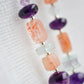 Mismatched gemstone long bar earrings shown in sterling silver. Stones include: amethyst, aquamarine, fluorite, and sunstone. Stones are set onto a long straight bar. Close up image.
