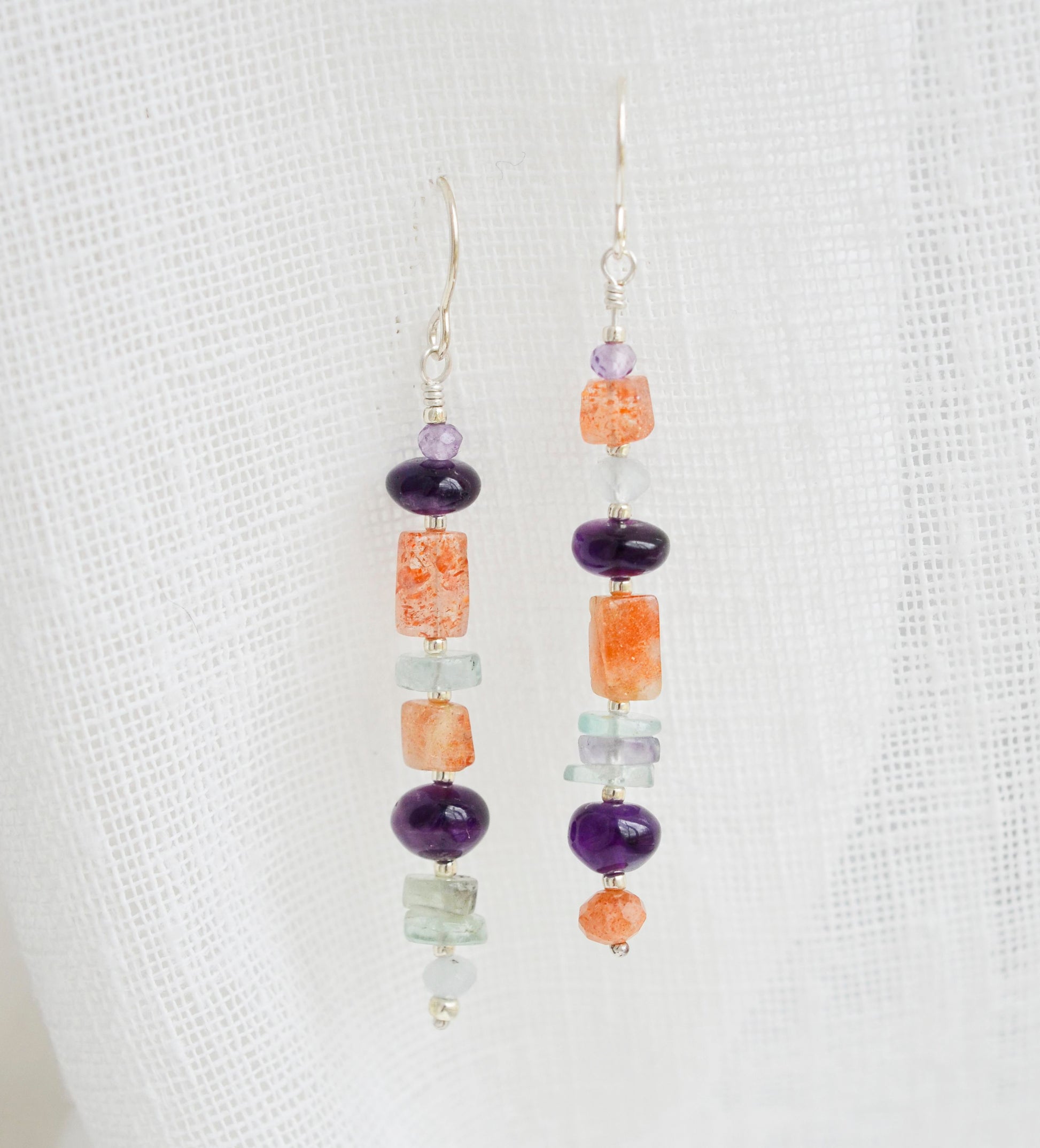 Mismatched gemstone long bar earrings shown in sterling silver. Stones include: amethyst, aquamarine, fluorite, and sunstone. Stones are set onto a long straight bar.