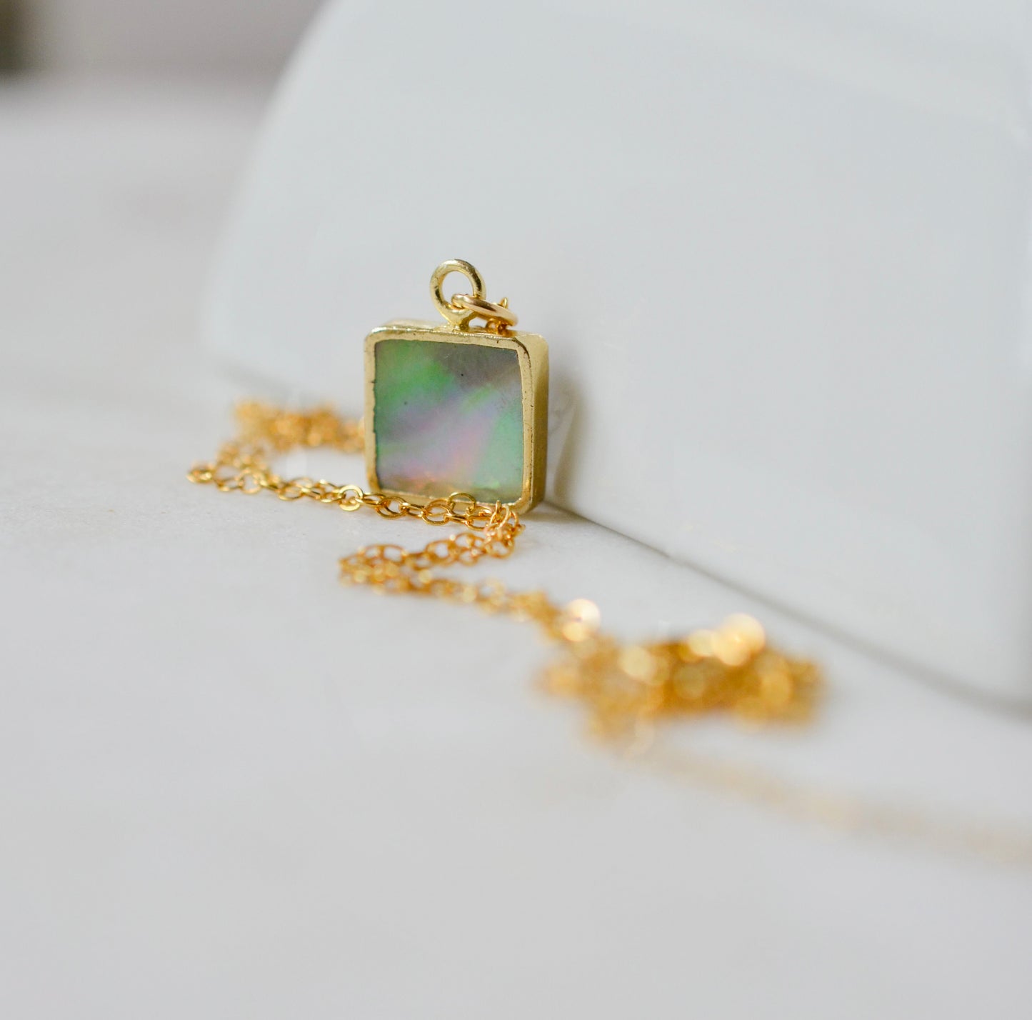 A natural minimalist mother of pearl square shaped pendant set on a 14k gold filled chain. This dainty necklace is handmade in Connecticut by Gemnia.