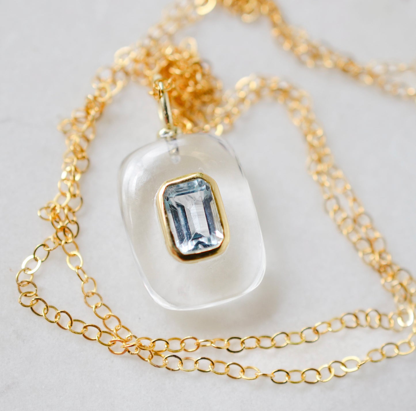 Close up image. Handmade Maris necklace featuring a Blue Topaz set inside a clear Rock Crystal frame on a 14K Gold Filled chain. Ideal gift for wife, girlfriend, or mom. Minimalist topaz pendant for layering.