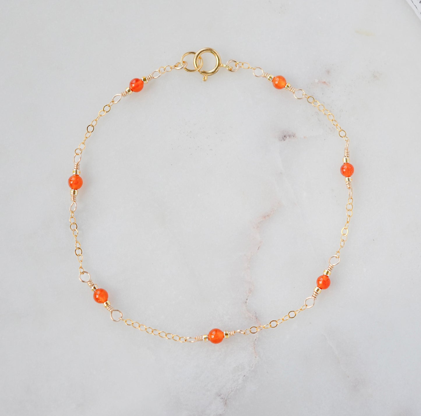 A gold-colored bracelet featuring orange carnelian stones on a 14k gold filled chain.