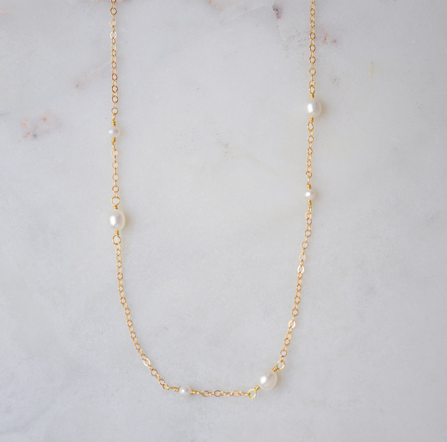 Gold necklace with small dainty pearls on a marble surface.