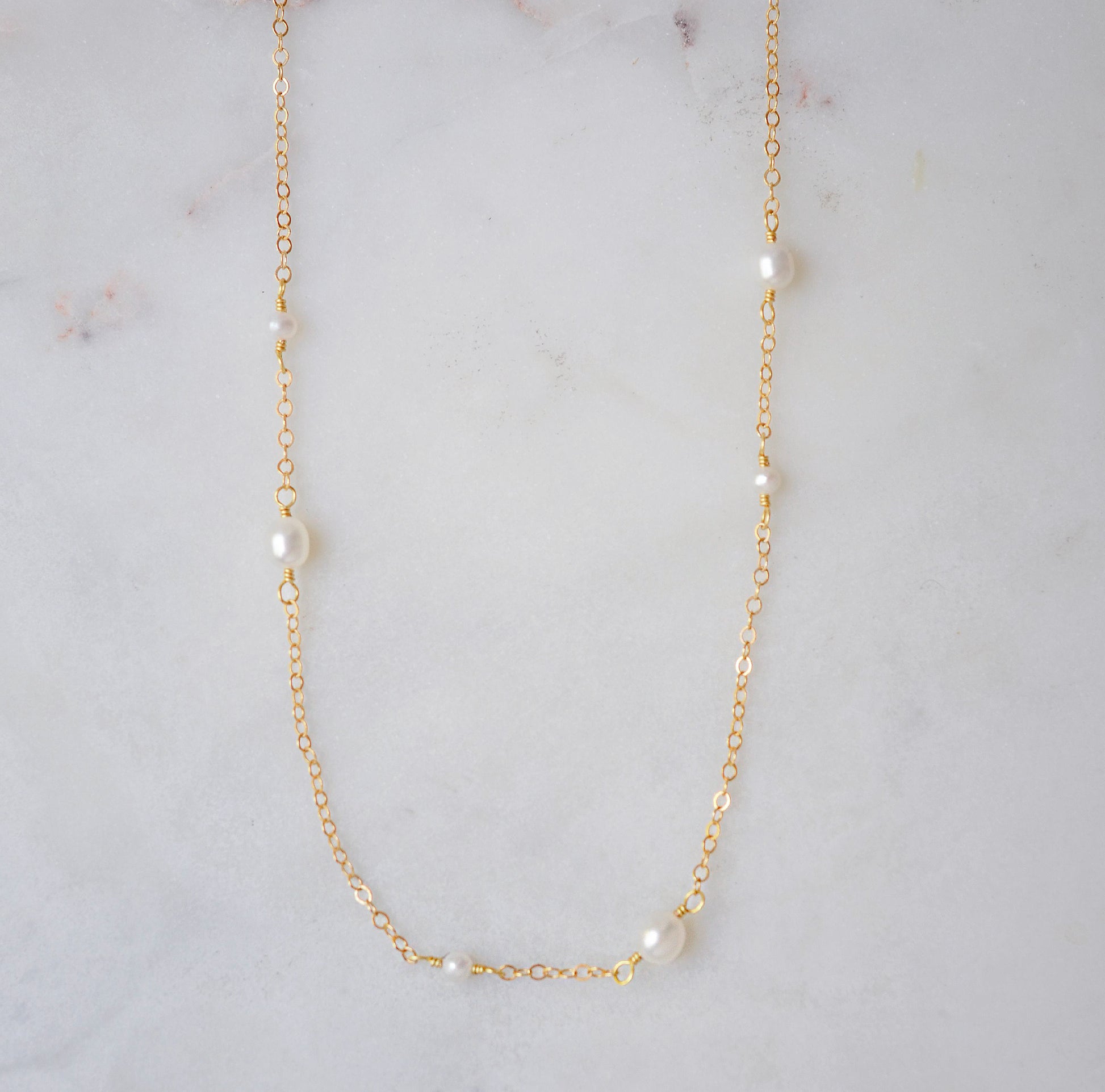 Gold necklace with small dainty pearls on a marble surface.