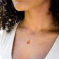 A woman wearing a natural, faceted orange Carnelian gemstone necklace with a 14k gold filled chain. The crystal is a triangular teardrop shape and ranges in shades of orange and sometimes red. Also available in sterling silver. Handmade in Connecticut by Gemnia.