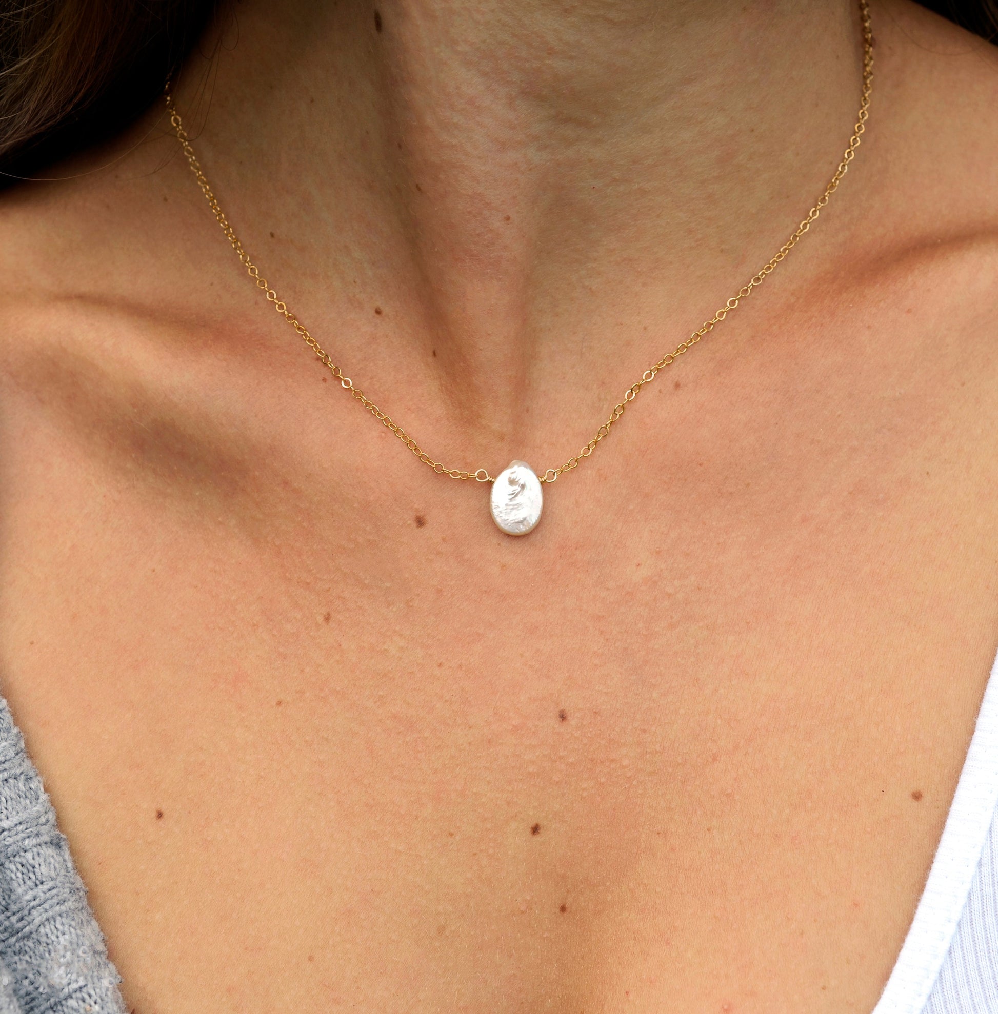 Single white oval shaped freshwater pearl suspended from a sterling silver or 14k gold filled cable chain. Modeled image.