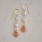 Two white semi-round pearls hang over natural peach Moonstone faceted drops. The gold style is shown.
