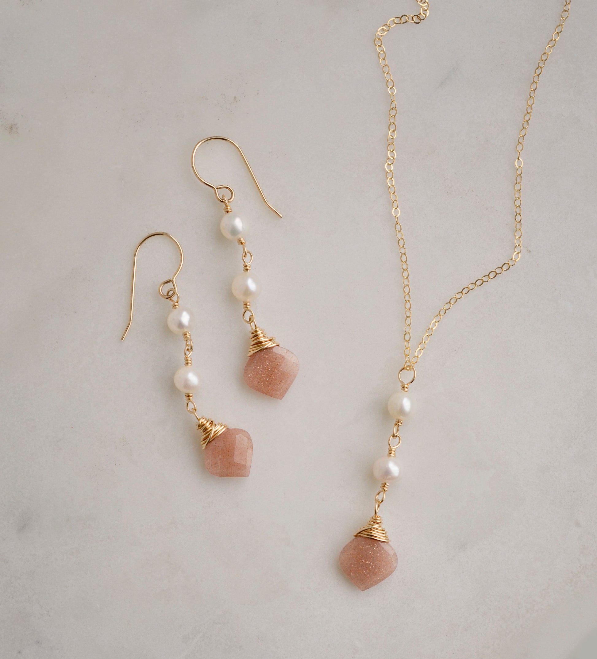 Two white semi-round pearls hang over natural peach Moonstone faceted drops. Shown with a matching necklace. The gold style is shown.