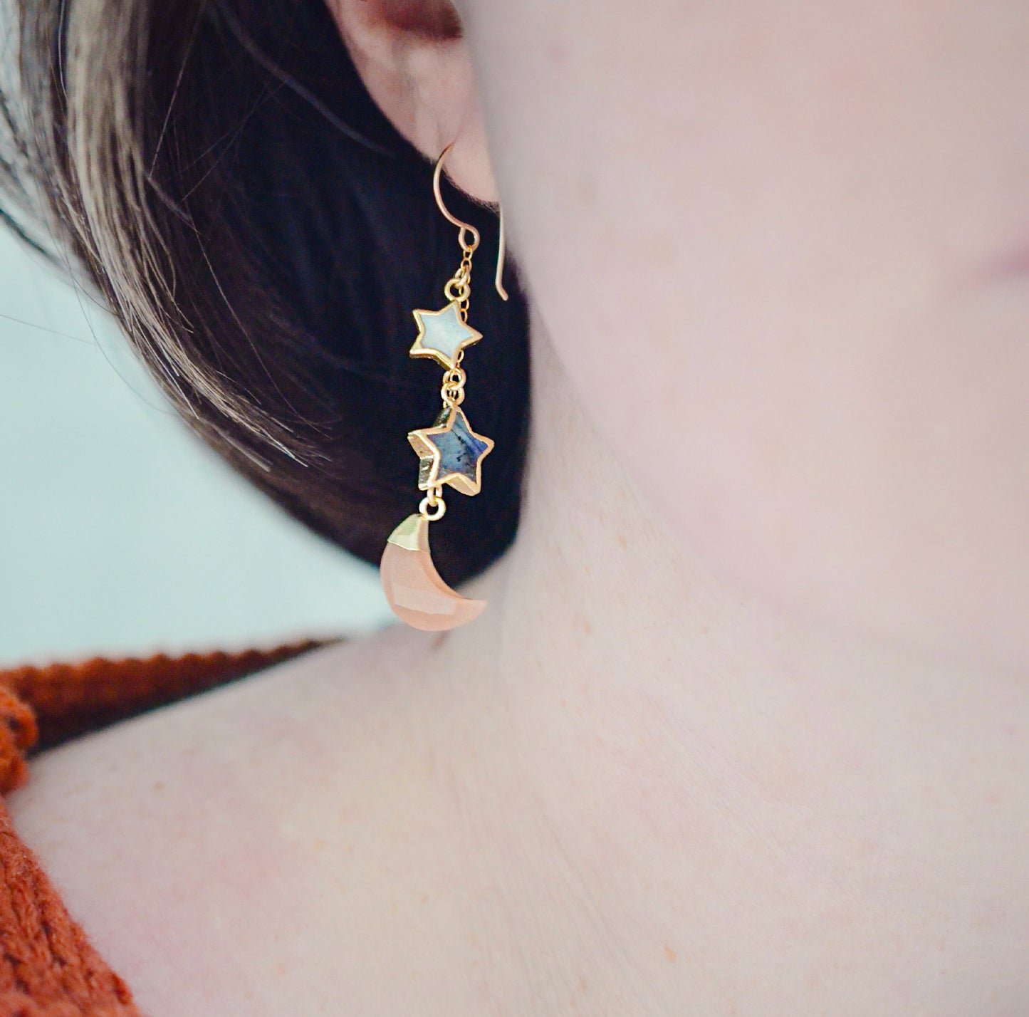 Mother of pearl, Labradorite, and Peach Moonstone moon and star dangle earrings in gold. Each earring has two stars hanging over a peach moonstone crescent. Modeled image.