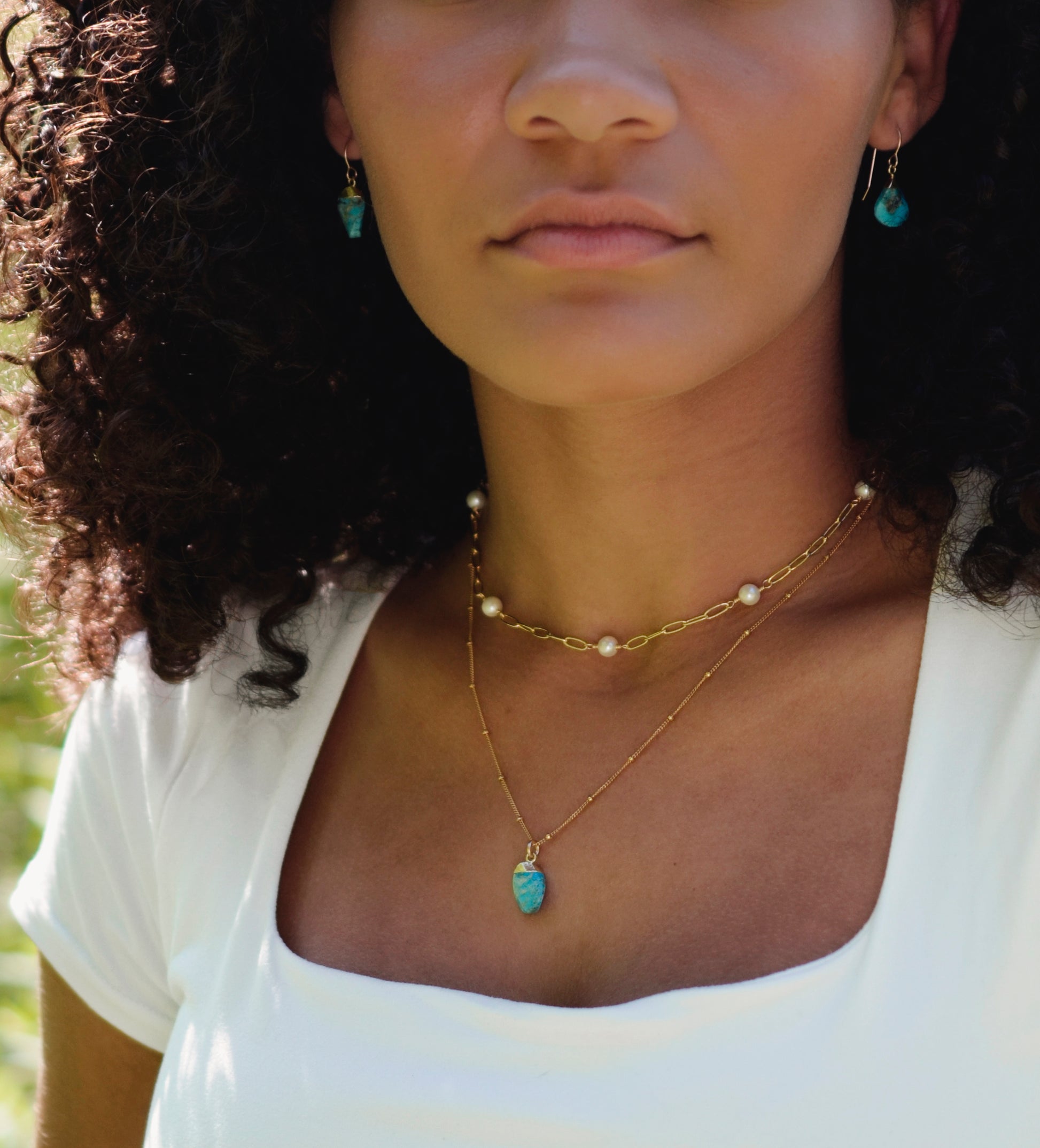 White freshwater pearls set onto a gold paperclip style chain. Modeled image. Necklace modeled with a turquoise pendant and earrings.