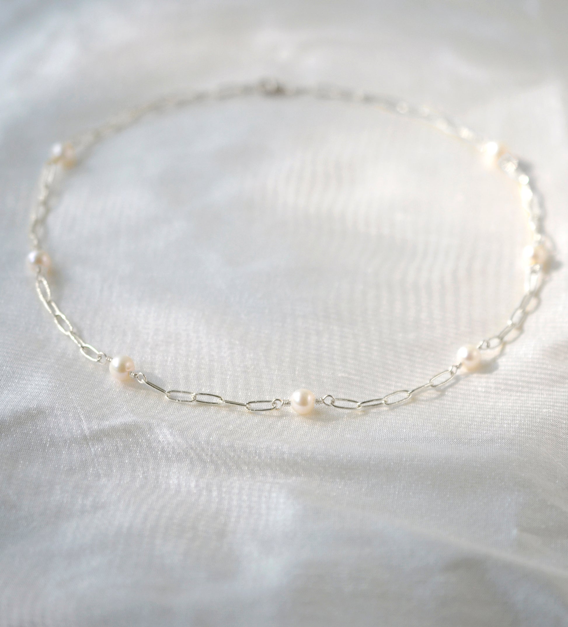 Seven white freshwater pearls set onto a silver paperclip style chain.