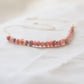 Natural pink Rhodochrosite beaded handmade necklace shown in 14k gold filled. The gemstones vary in shades of pink, peach, white, and gray and are faceted rondelle shape. They span approximately 4 inches across the front of the necklace, then attach to a dainty cable chain. Also available in sterling silver.