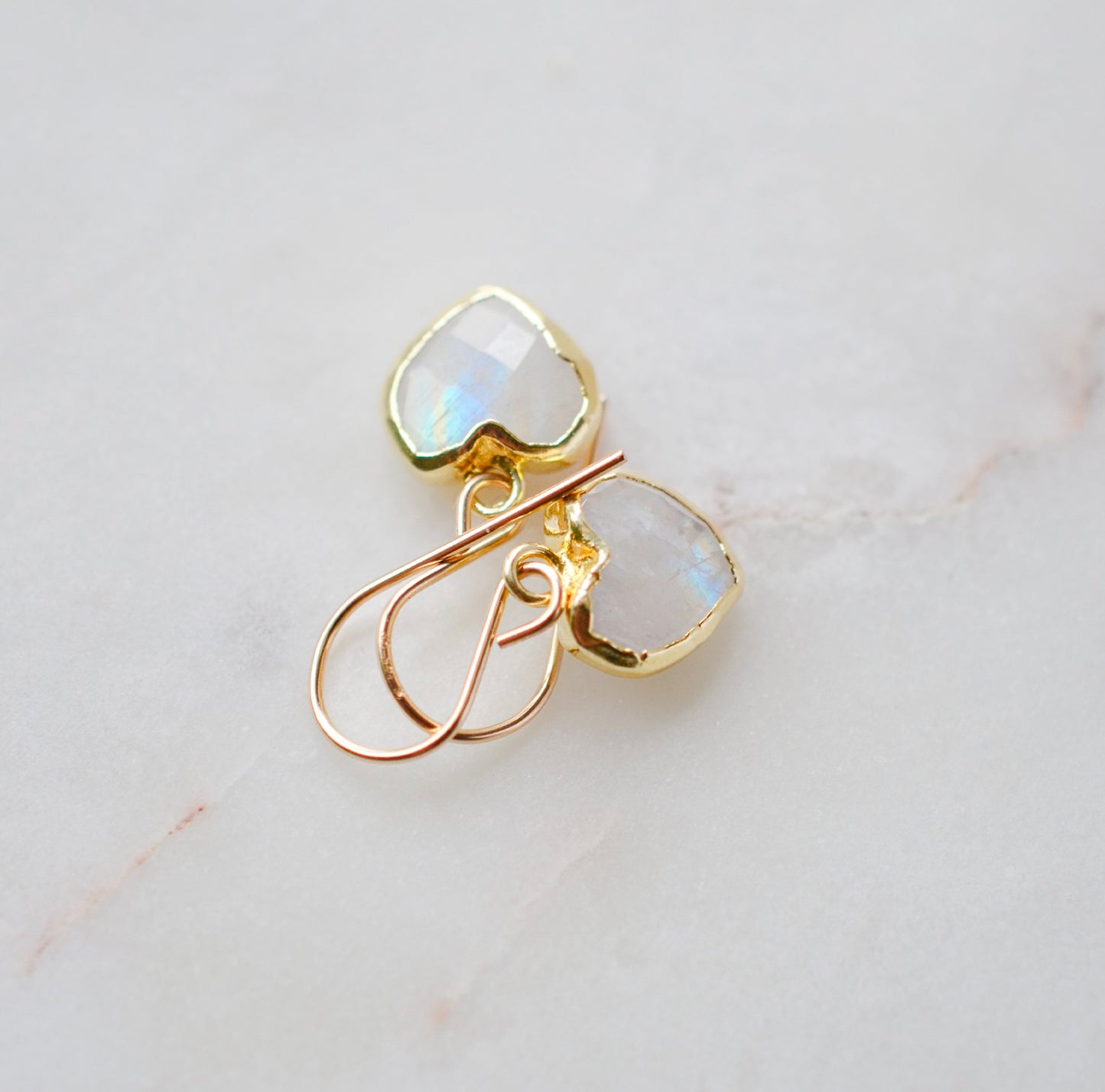 Natural rainbow moonstone stone heart earrings in gold. The stones are white, but flash blue with movement.