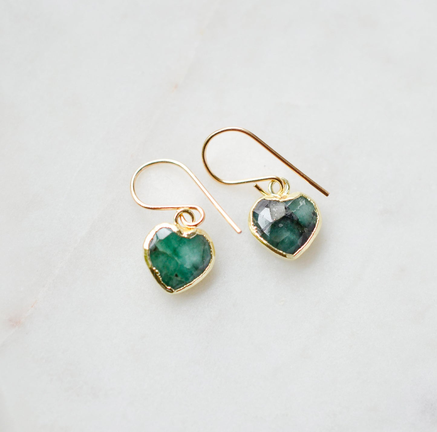 Raw emerald heart earrings in gold. The stones are bezeled in 22k gold then set on gold earwires. The gemstone colors range in dark greens with hints of white or black.