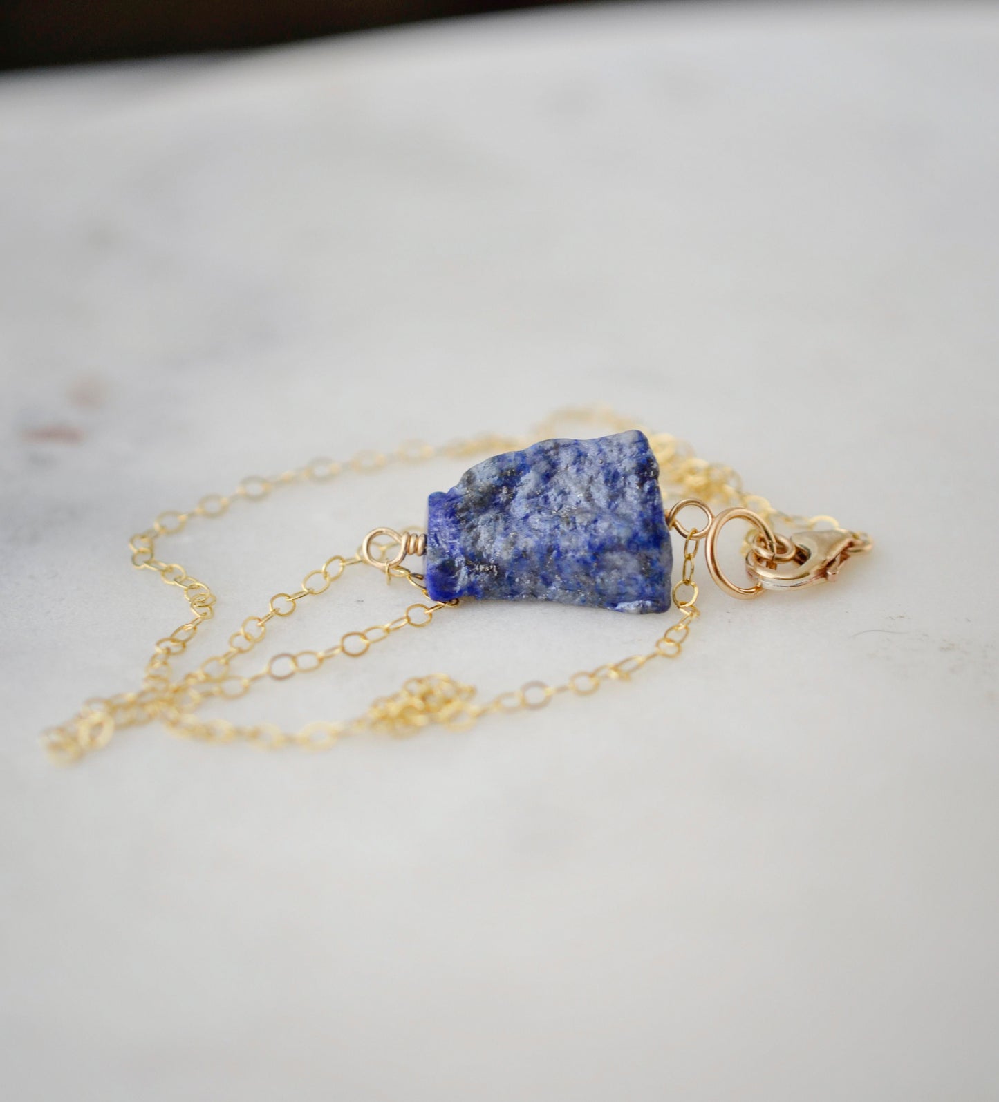 Raw blue lapis lazuli stone suspended from a gold chain.