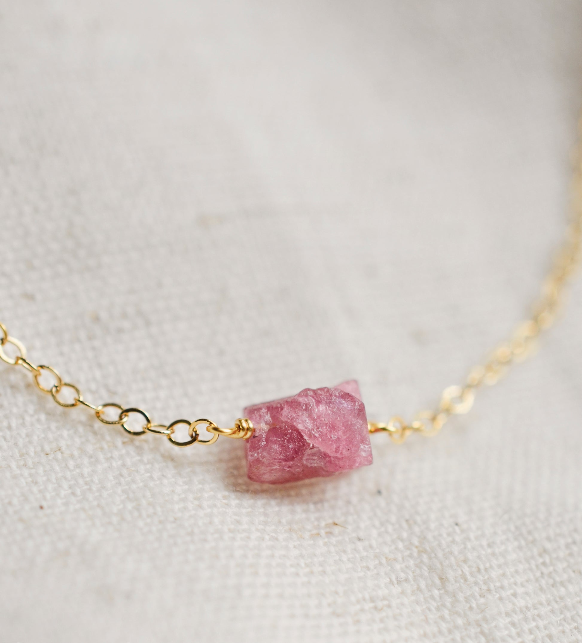 A close up of a minimalist pink tourmaline crystal set onto a 14k gold filled chain. 