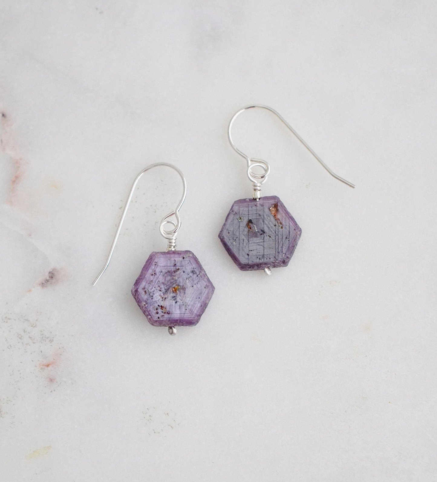 Purple-pink raw ruby stones suspended from sterling silver earwires. The stones are rough and in their natural hexagonal shape. 
