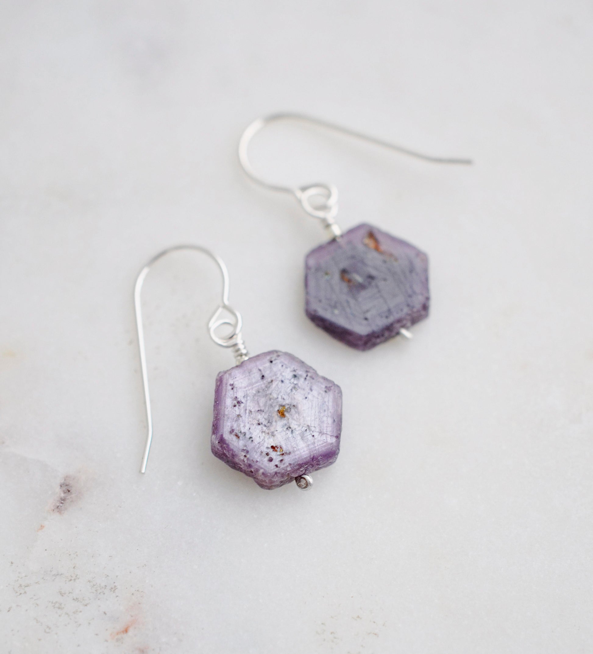 Purple-pink raw ruby stones suspended from sterling silver earwires. The stones are rough and in their natural hexagonal shape. 