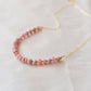 Natural pink Rhodochrosite beaded handmade necklace shown in 14k gold filled. The gemstones vary in shades of pink, peach, white, and gray and are faceted rondelle shape. They span approximately 4 inches across the front of the necklace, then attach to a dainty cable chain. Also available in sterling silver.
