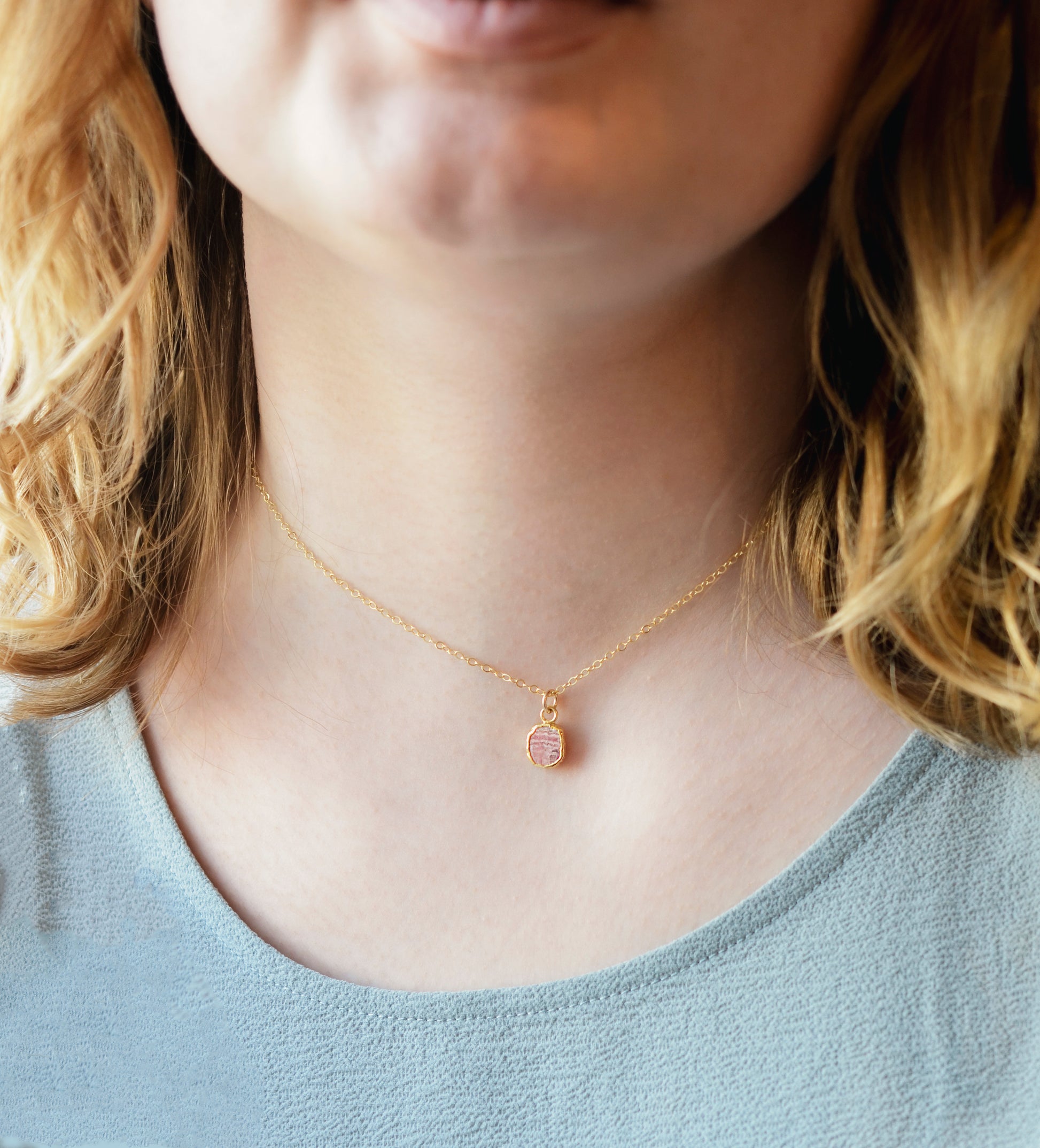 Pale pink Rhodochrosite smooth polished slice set in gold. Shown on a gold chain. Modeled image.