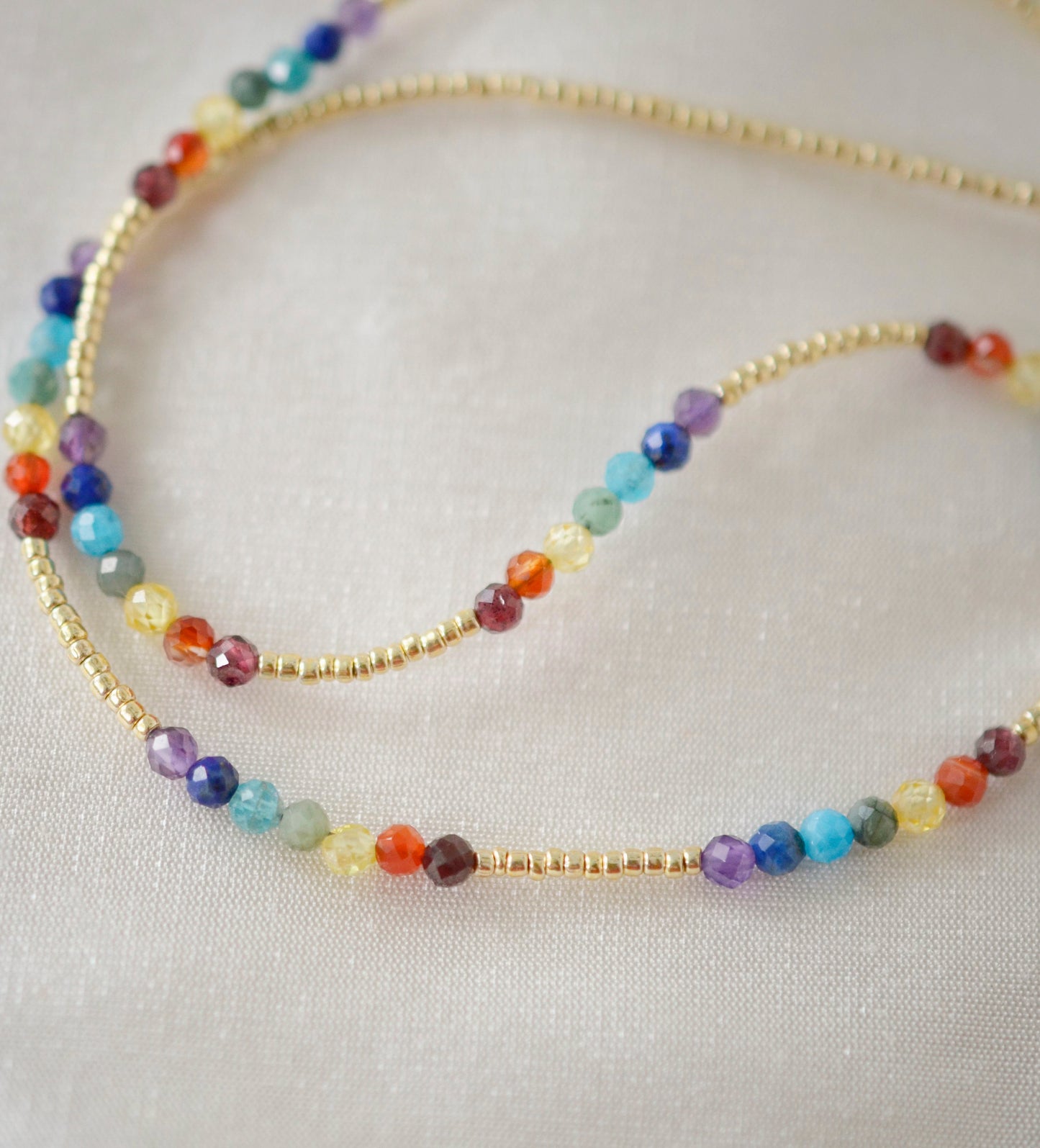 Tiny stones arranged in the order of the seven chakras or rainbow colors. Colors include: purple, blue, aqua, green, yellow, orange, and red. Close up of the gold style.