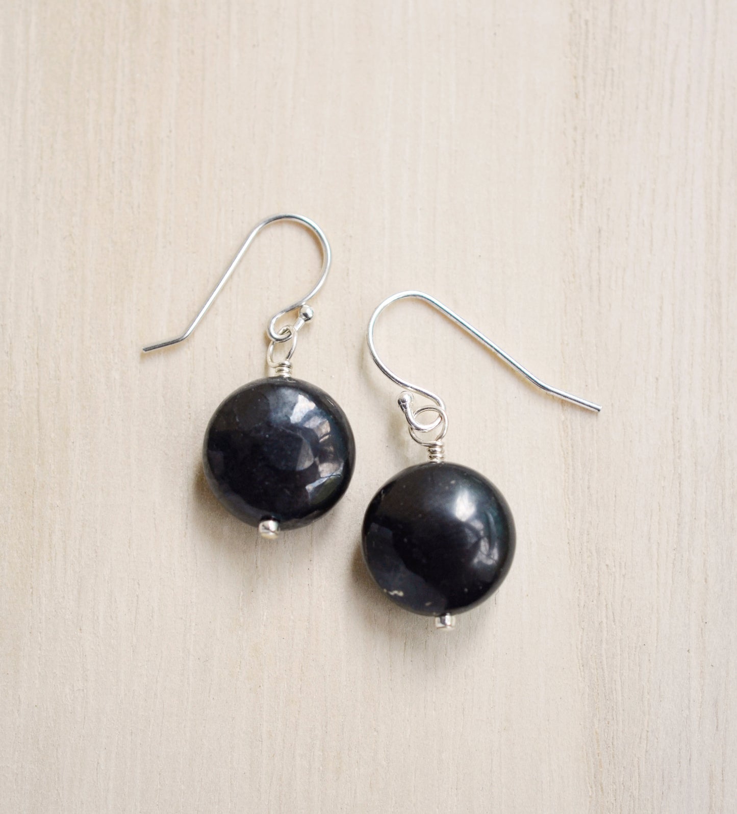 Natural smooth polished coin shape black Shungite dangle from sterling silver earring hooks. 