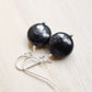 Natural smooth polished coin shape black Shungite dangle from sterling silver earring hooks.