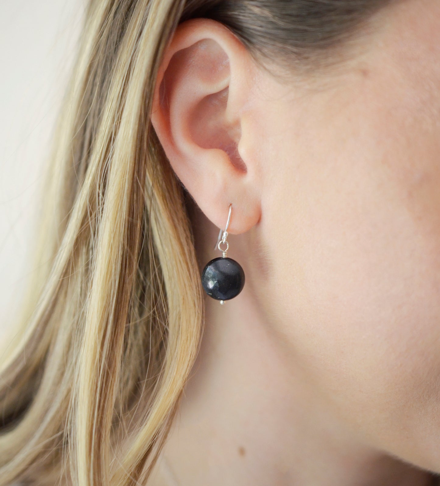 Natural smooth polished coin shape black Shungite dangle from sterling silver earring hooks. Modeled image. 