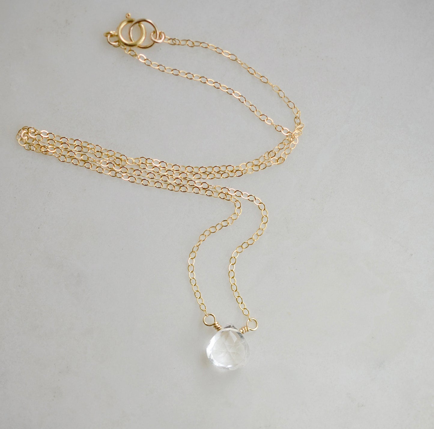 A clear, natural crystal quartz faceted teardrop set onto a 14k gold filled chain.