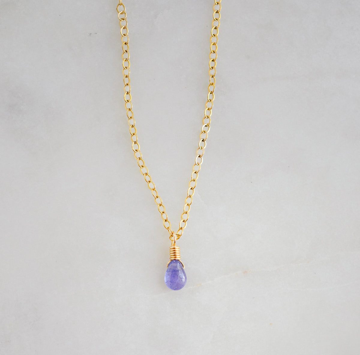 An image of a smooth polished natural, real tanzanite gemstone teardrop suspended from a 14k gold filled chain. Also available in sterling silver. Handmade in Connecticut by Gemnia.