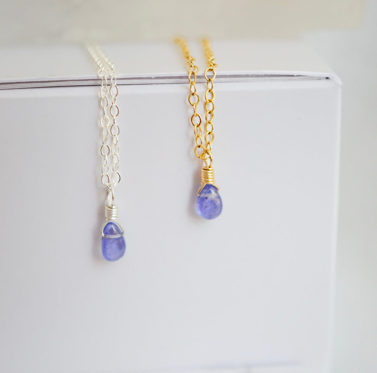 Close up of two real tanzanite pendants on sterling silver or 14k gold filled chains. The crystals are smooth polished and ultra dainty.