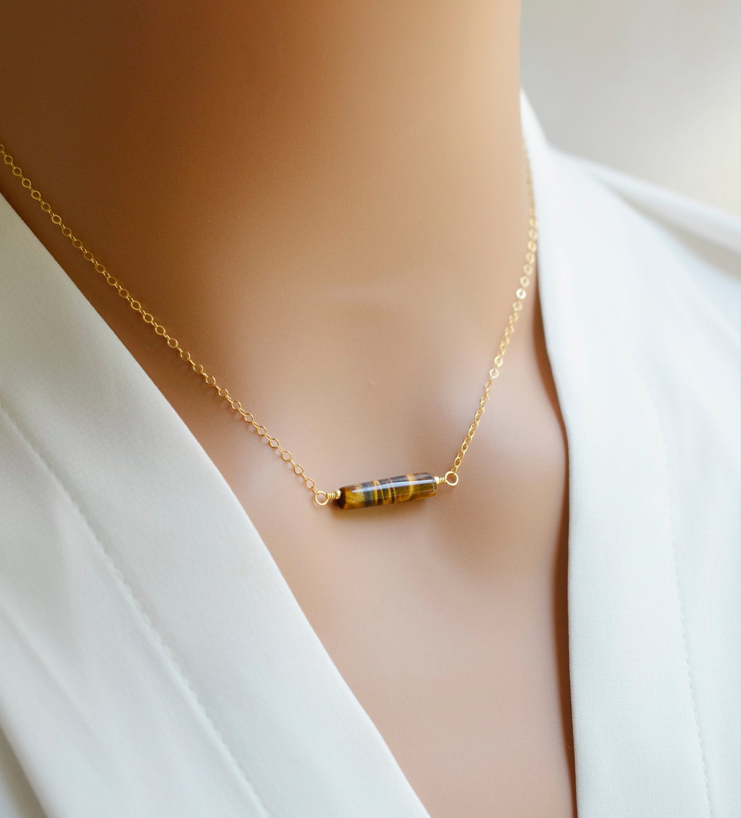 Tiger Eye gemstone necklace. A smooth polished Tiger Eye stone in a bar or tube shape set onto a 14k gold filled chain. Modeled image.