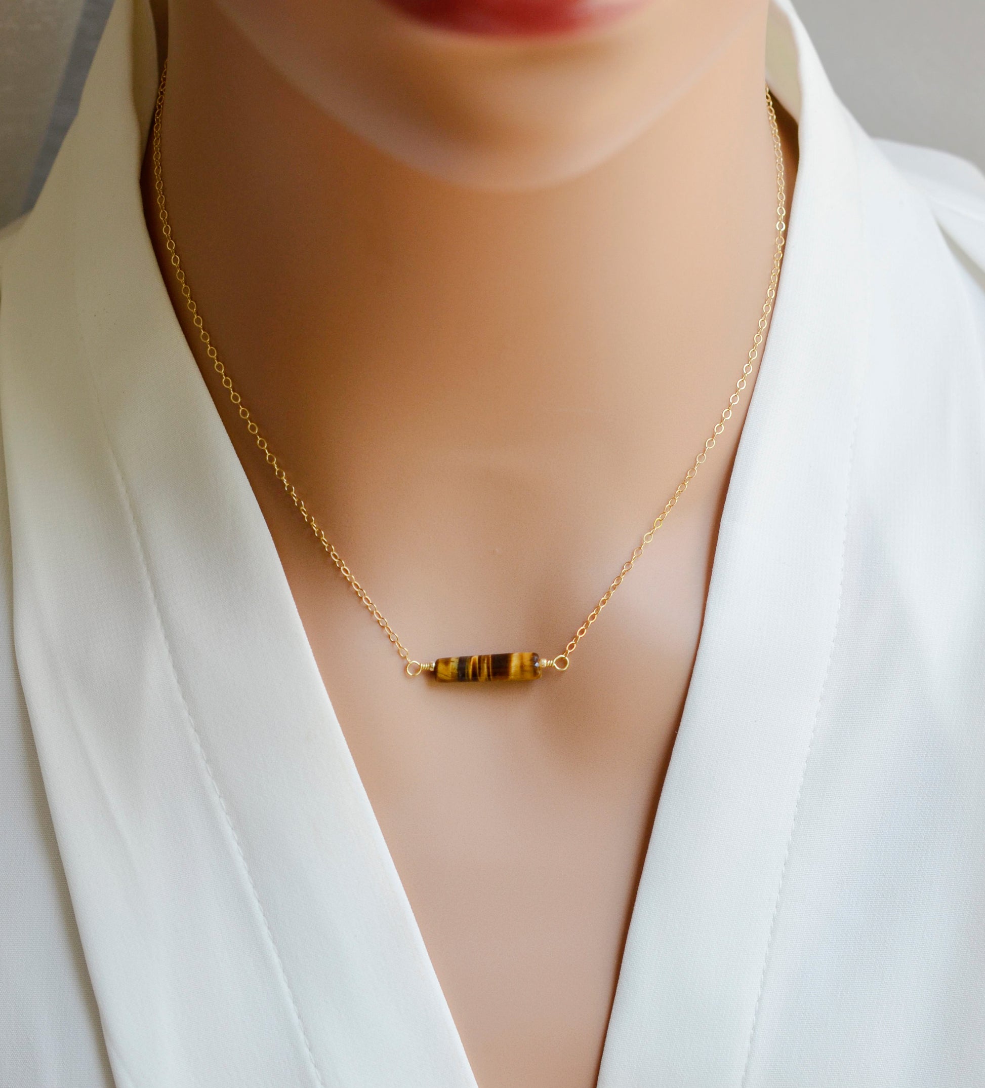 Tiger Eye gemstone necklace. A smooth polished Tiger Eye stone in a bar or tube shape set onto a 14k gold filled chain. Modeled image.