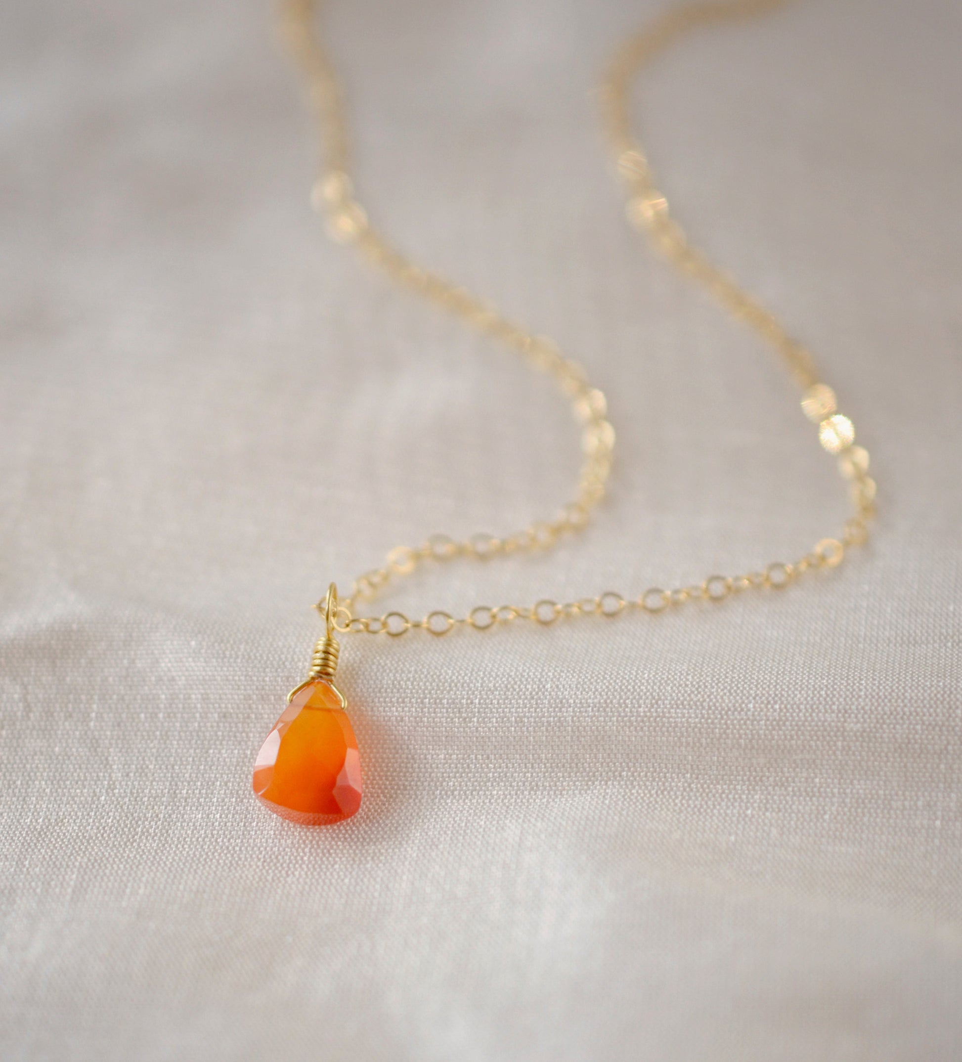 Natural orange triangular shaped Carnelian gemstone set onto a gold chain. Stones vary in color from orange to red.