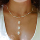 Three white cowrie shells hang from a 14k gold filled chain. Modeled with a beaded pearl necklace.