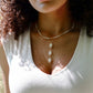 Three white cowrie shells hang from a 14k gold filled chain. Modeled with a beaded pearl necklace.