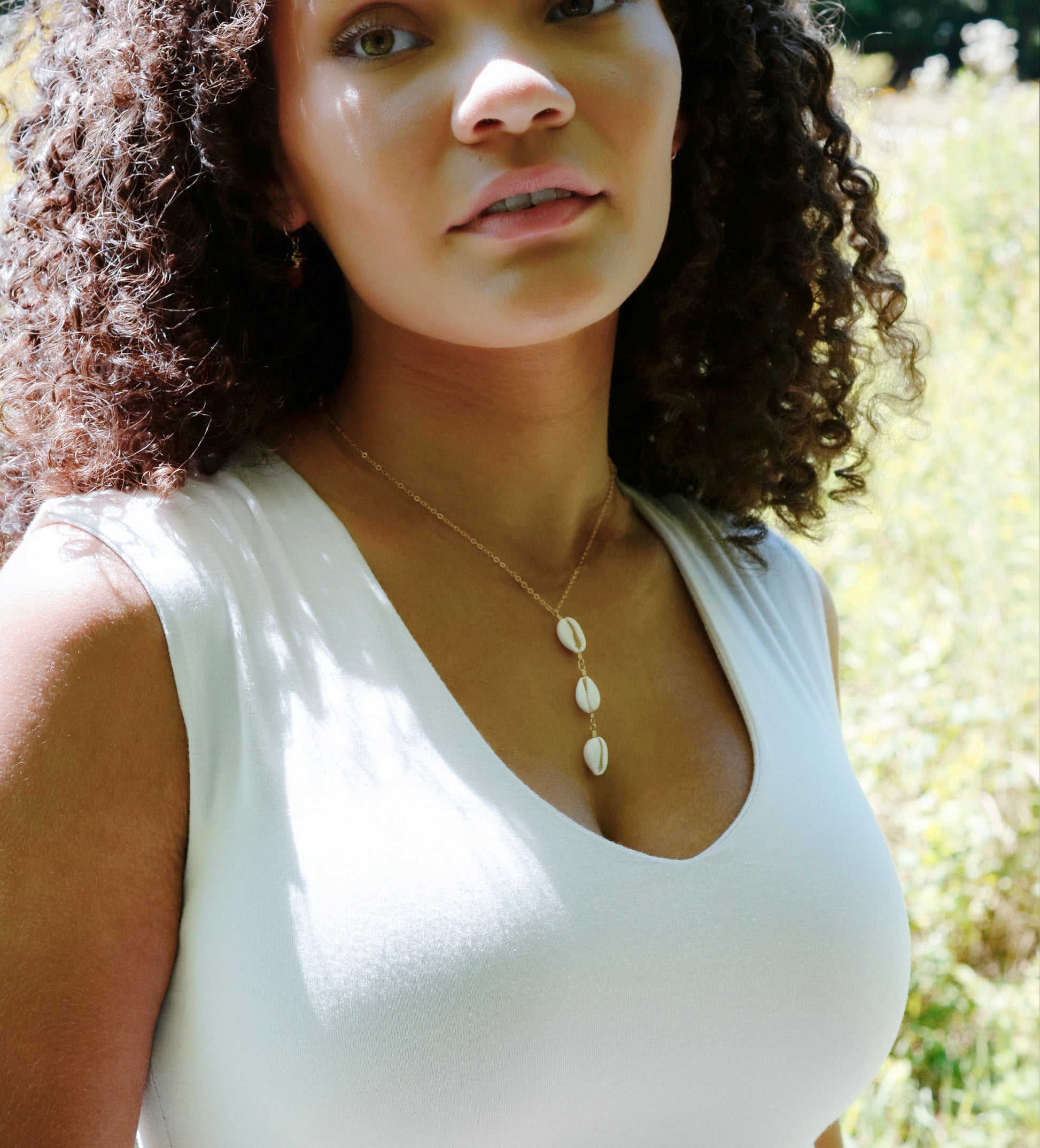 Three white cowrie shells hang from a 14k gold filled chain. Modeled image.