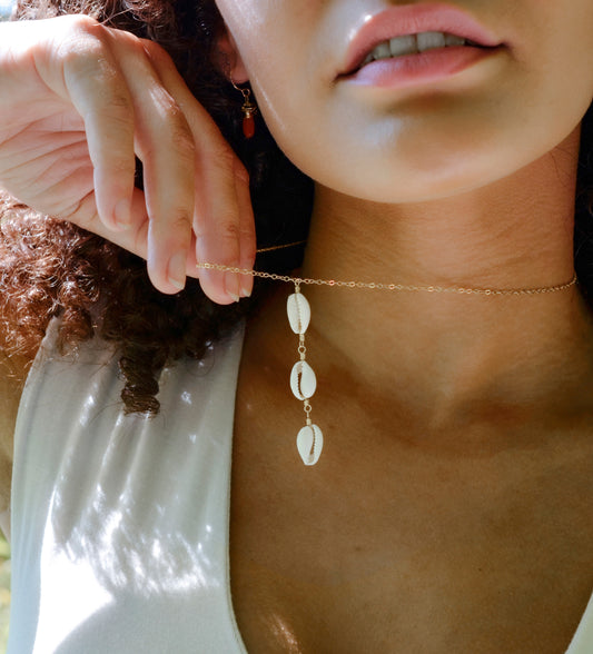 Three white cowrie shells hang from a 14k gold filled chain. 