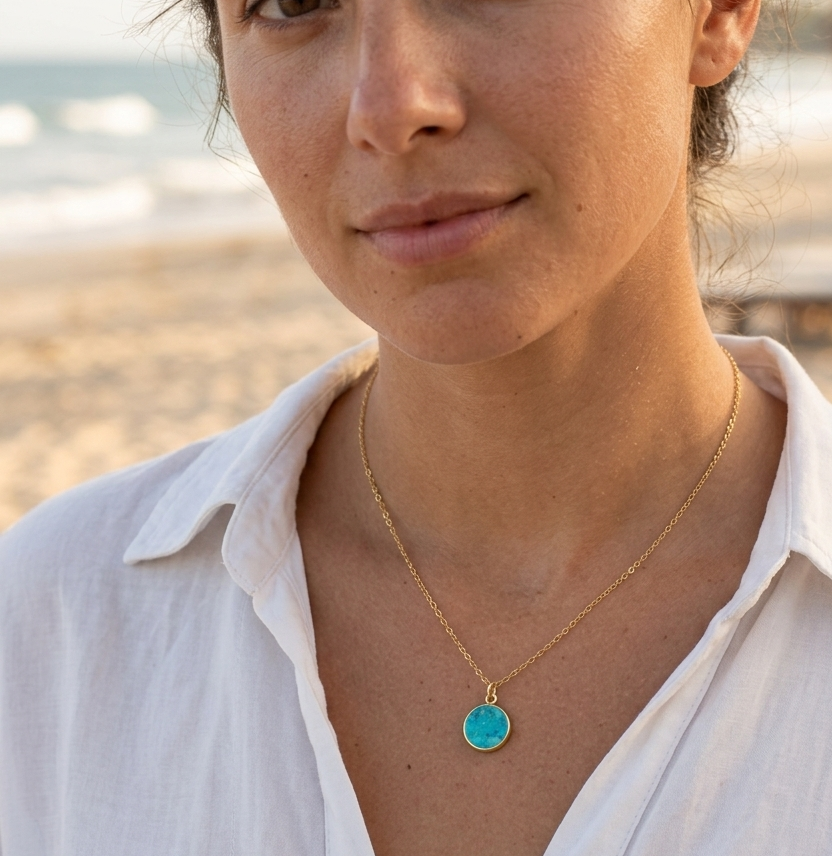 Woman wearing a gold necklace with a turquoise stone pendant. This jewelry is handmade in Connecticut by Gemnia.