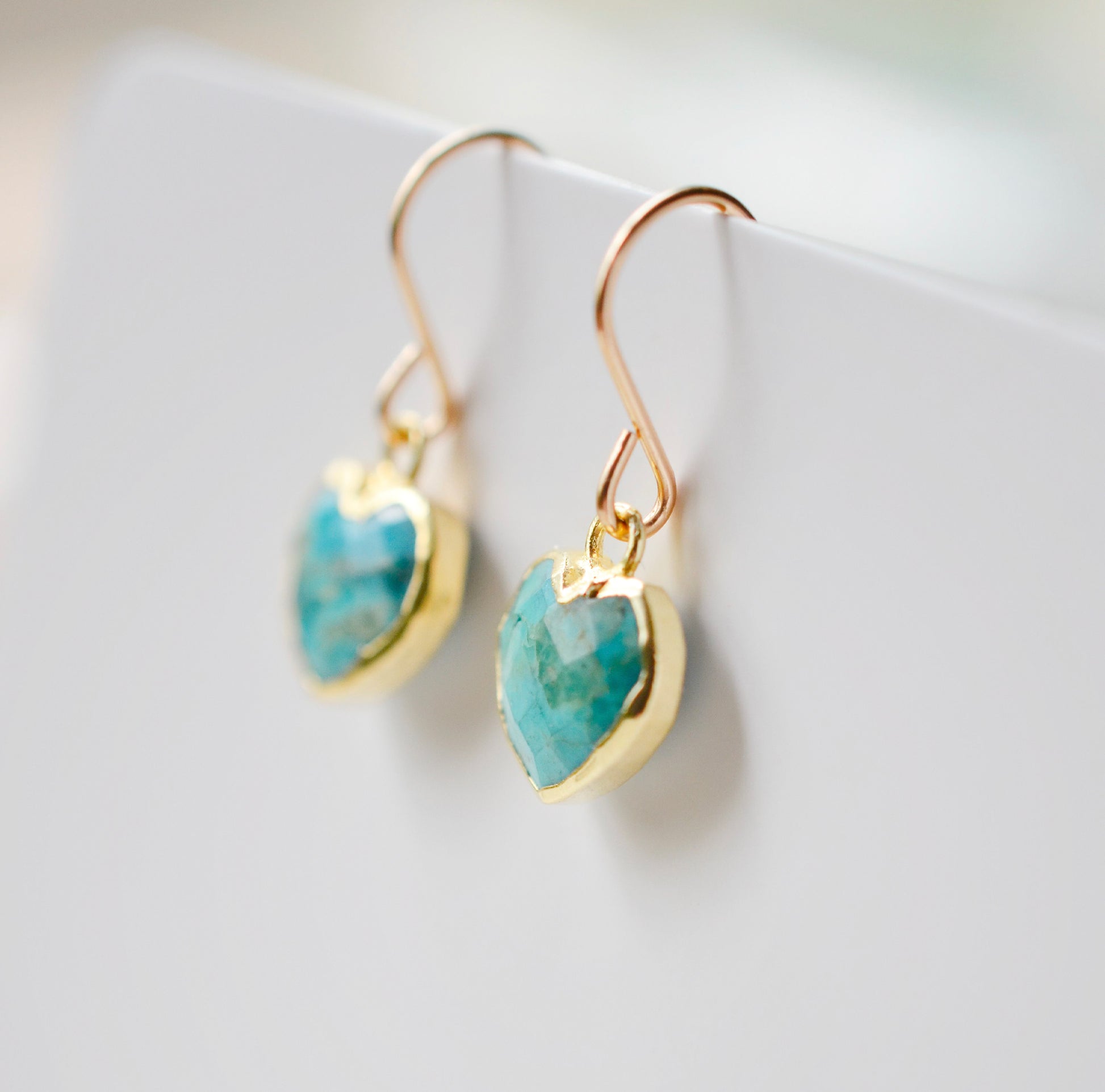 Genuine, natural blue turquoise faceted hearts set on 14k gold filled earring hooks. The stones range in blue and green, with some containing white or brown. Side view.