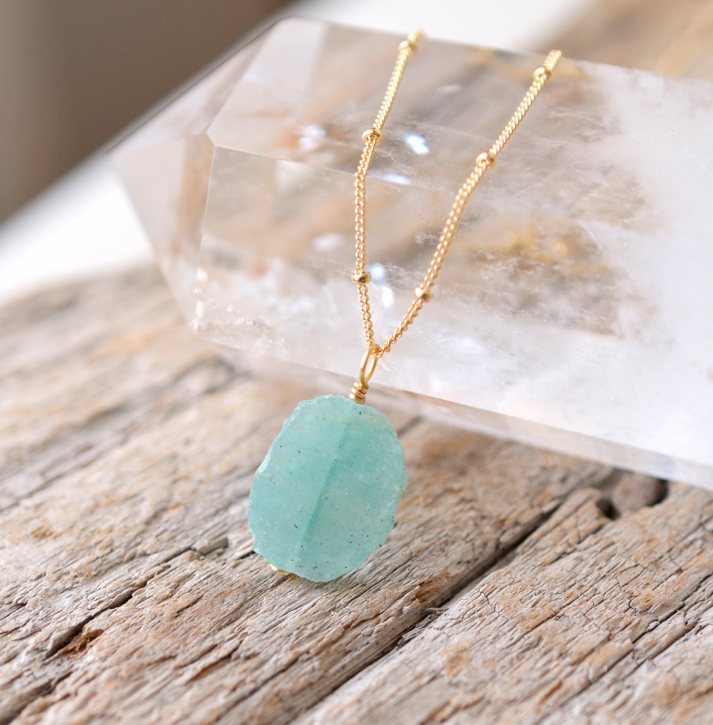 Aqua blue amazonite slice gemstone set onto a beaded 14k gold filled chain. The stone is semi oval in shape, but irregular. It's smooth polished, but with raw edges. 