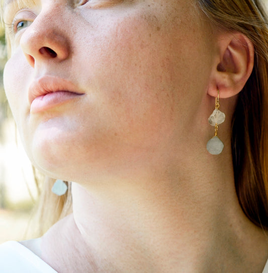 Raw clear quartz and blue Aquamarine gemstones dangle from gold filled earring hooks. Modeled Image.