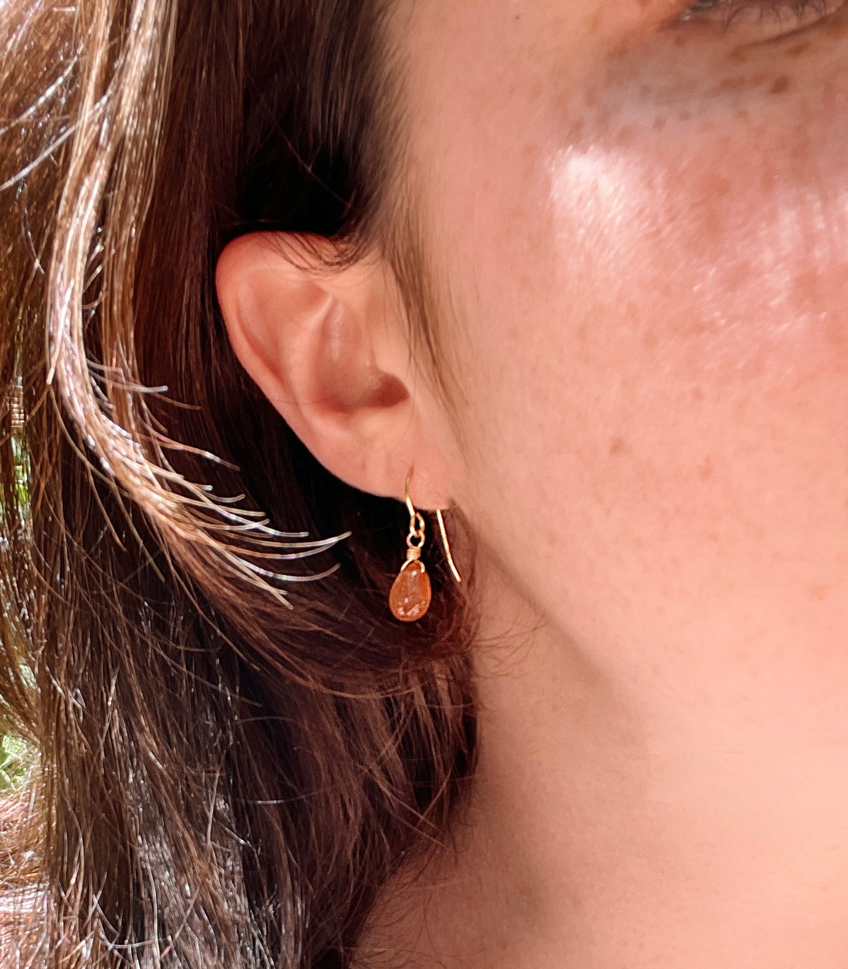 Genuine orange sunstone teardrop dangle earrings shown in 14k gold filled. The gemstones are smooth polished. Modeled image.