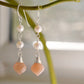 Two white semi-round pearls hang over natural peach Moonstone faceted drops. The silver style is shown.
