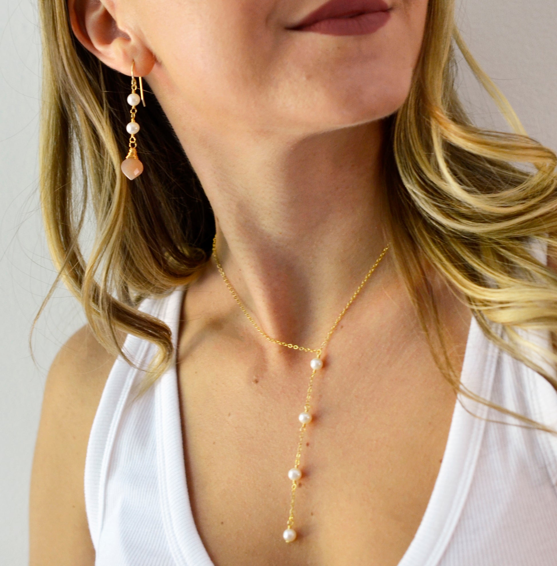 Two white semi-round pearls hang over natural peach Moonstone faceted drops. The gold style is shown. Modeled image.
