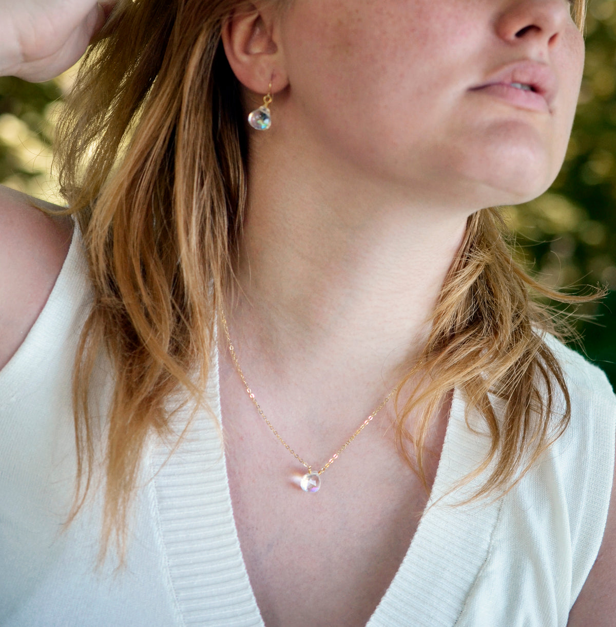 A woman wearing a Mystic Topaz crystal pendant and earring set in 14k gold filled. The gemstones are clear, but shift rainbow iridescent colors with movement. Handmade in Connecticut.