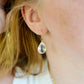 A woman wearing a rainbow mystic topaz faceted teardrop dangle earring in 14k gold filled. The crystals are clear, but contain rainbow colors that shift with movement. Handmade gemstone jewelry by Gemnia. 