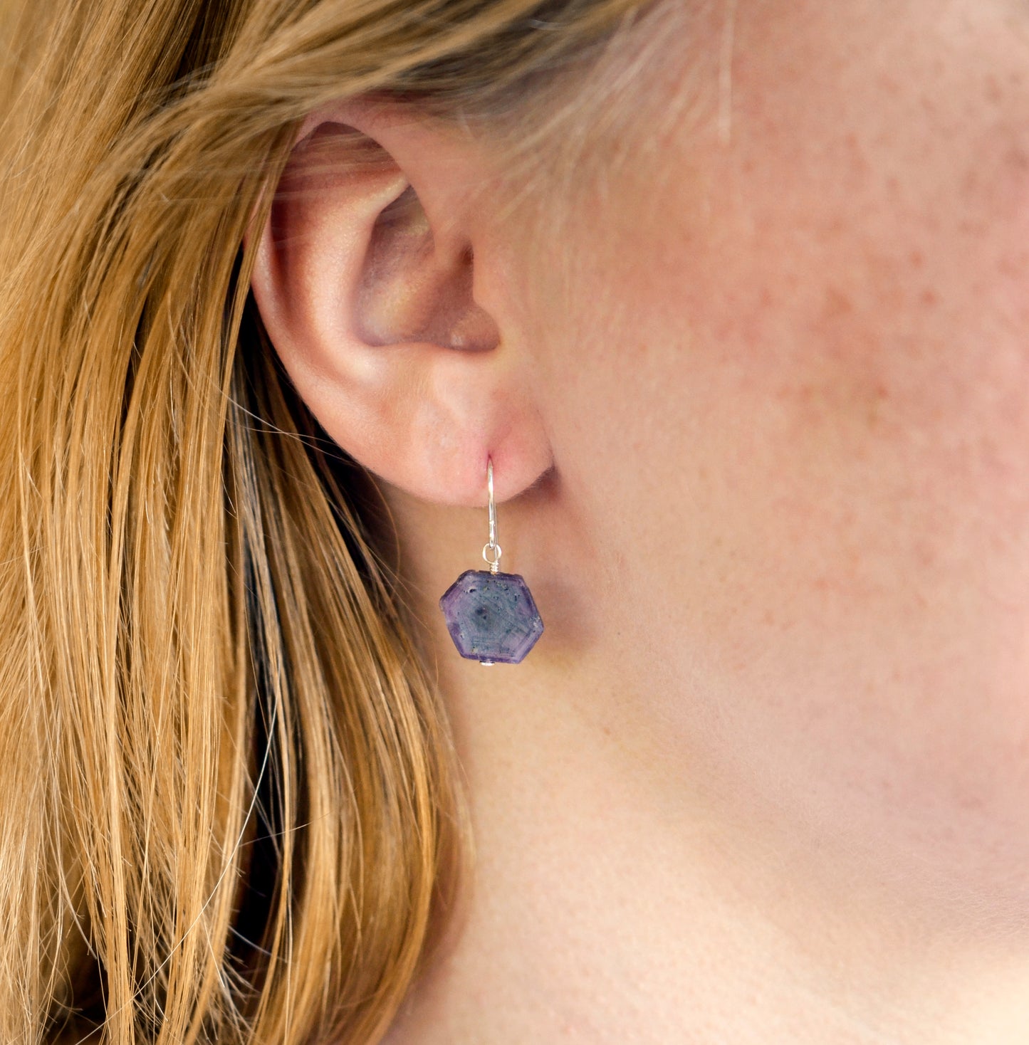 Purple-pink raw ruby stones suspended from sterling silver earwires. The stones are rough and in their natural hexagonal shape. Modeled image.
