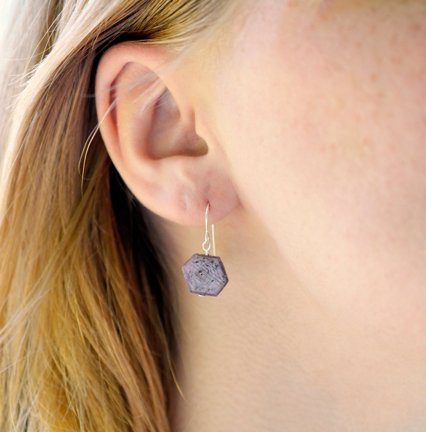 Purple-pink raw ruby stones suspended from sterling silver earwires. The stones are rough and in their natural hexagonal shape.  Modeled image.