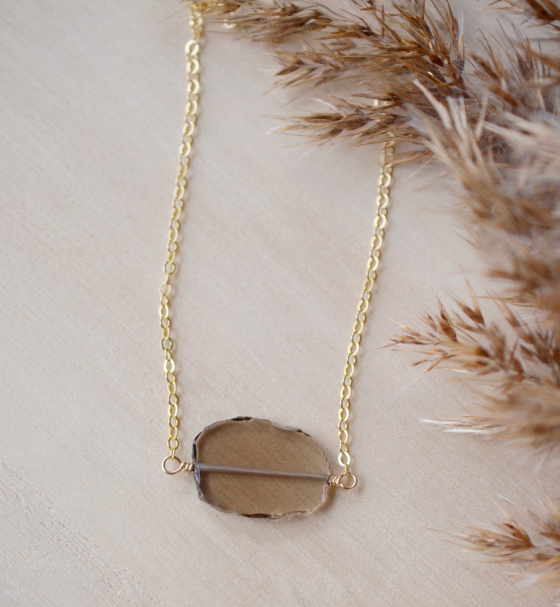 An irregular oval shape, smooth polished Smokey Quartz stone set onto a 14k gold filled chain. The stones edges are raw and irregular. 