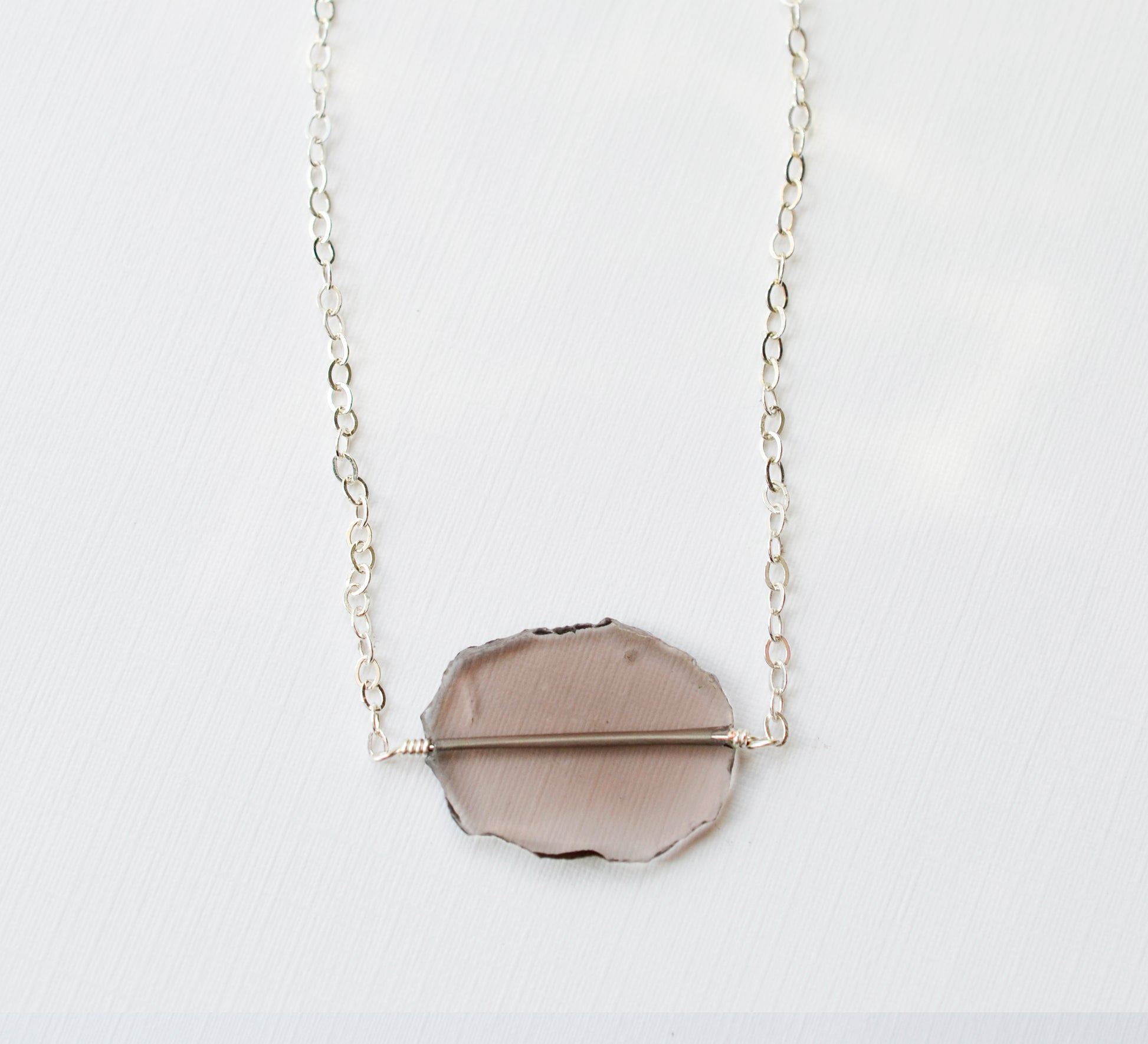 An irregular oval shape, smooth polished Smokey Quartz stone set onto a 14k gold filled chain. The stones edges are raw and irregular. The stone is mostly clear and may show natural inclusions.